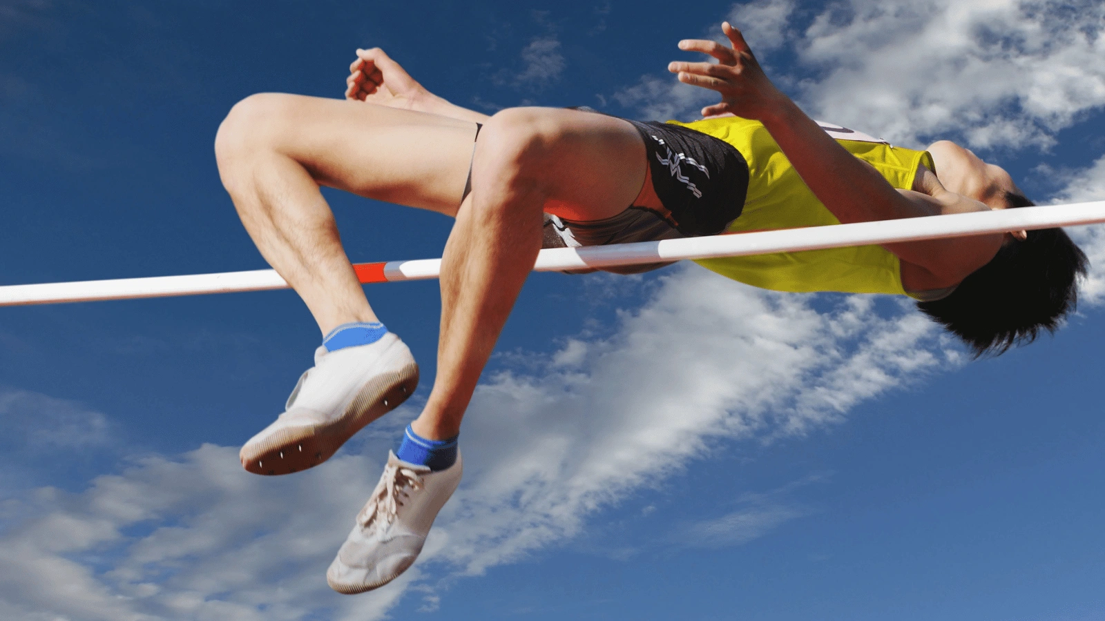Athlete performing a high jump under a blue sky perfect for action shots for sporting goods in an outdoor event.
