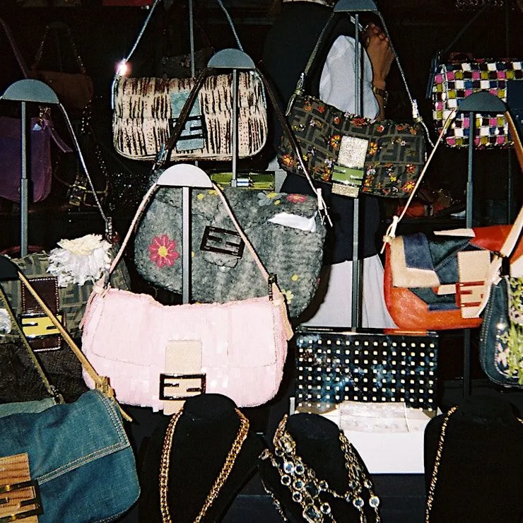 A display at the Manhattan Vintage Show 2025 featuring vintage handbags and gold jewelry on stands with a pink floral bag in the foreground.